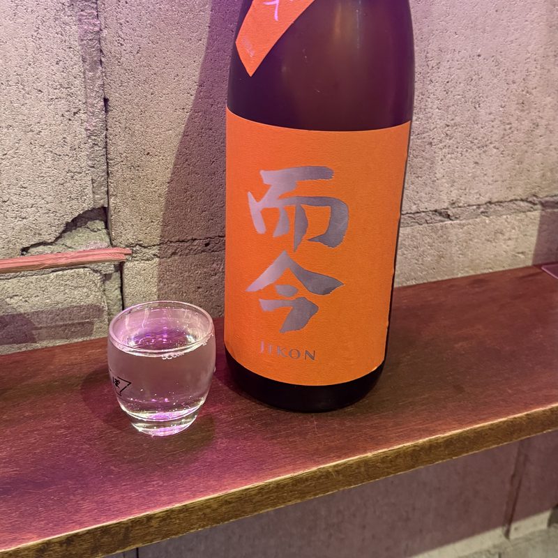 紫の照明の店に置かれた而今と、注がれた猪口